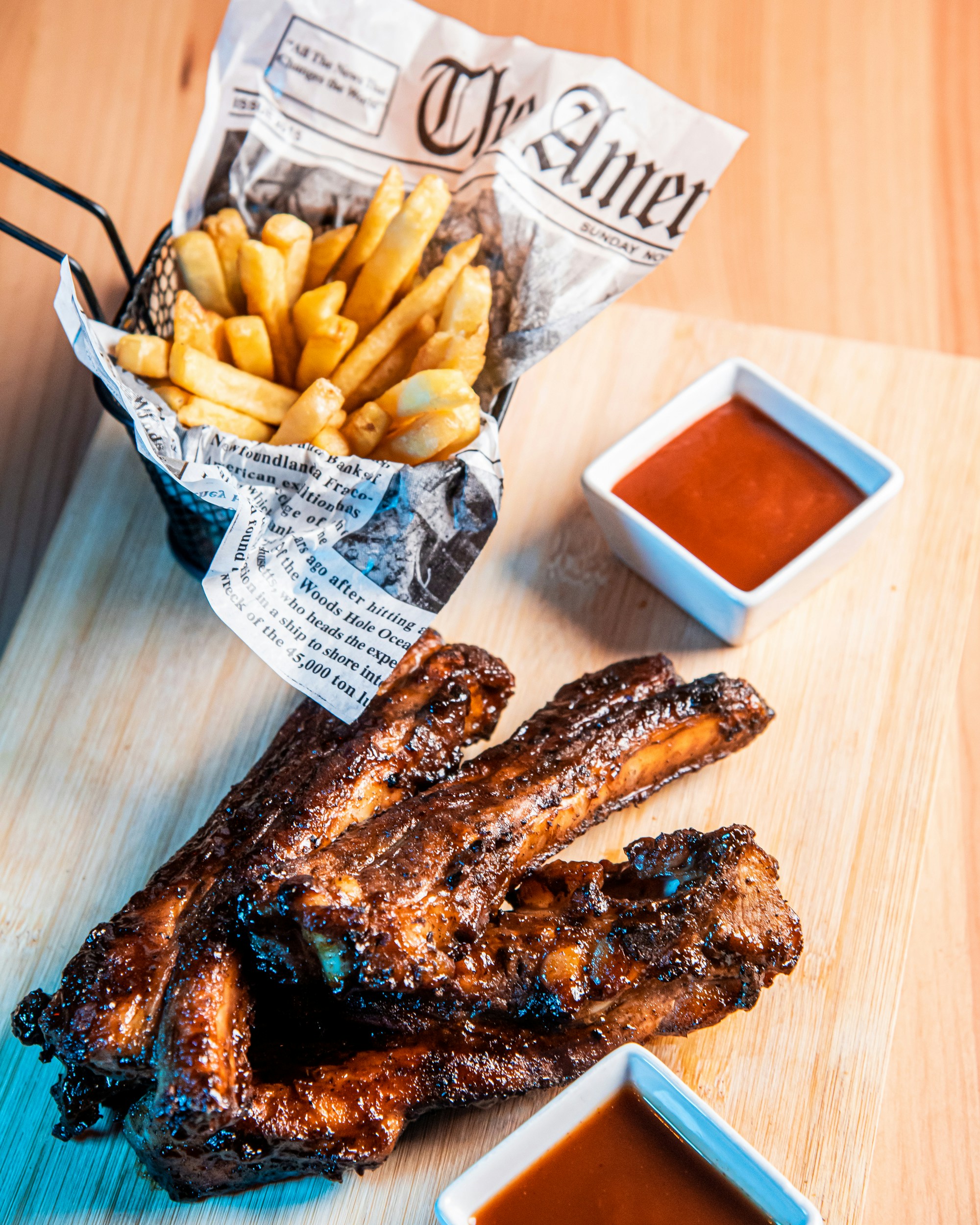 A wooden cutting board topped with ribs and french fries